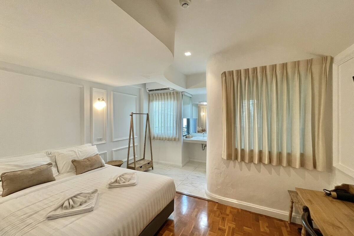 Un dormitorio espacioso con una cama grande, un columpio de madera, un baño con espejo y vistas a la ciudad.