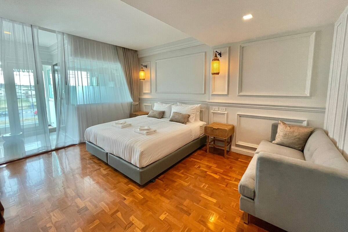 Habitación de hotel con una cama grande, un sofá, una mesita y vistas al exterior.
