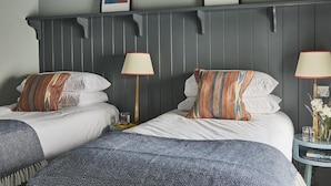 A hotel room with two beds, each with striped pillows, a grey headboard, and two bedside lamps. There are framed artworks on the wall above the beds.