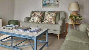 A living room with a sofa, a coffee table with books, a lamp, and a painting on the wall.
