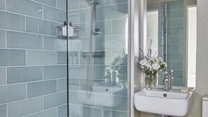 A bathroom with a glass-enclosed shower, a sink with a mirror above it, and patterned floor tiles.