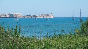 A coastal view with a fortified building, boats, and greenery.