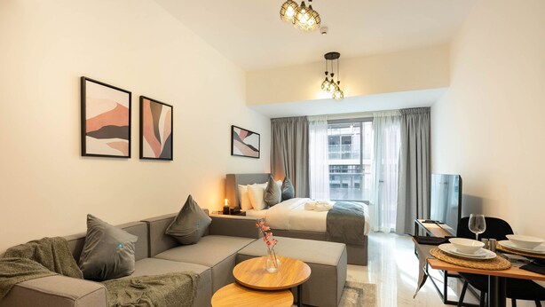 A modern hotel room with a sofa, a small round table, a bed, a dining area, and artwork on the walls. - Spacious Studio in Oasis 714 (Abu Dhabi)