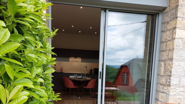 En patio med træterrasse, orange stole og en glasdør, der fører til et spiseområde indendørs.