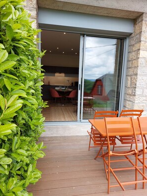 A patio area with a wooden deck, orange chairs, and a glass door leading to an interior dining space.