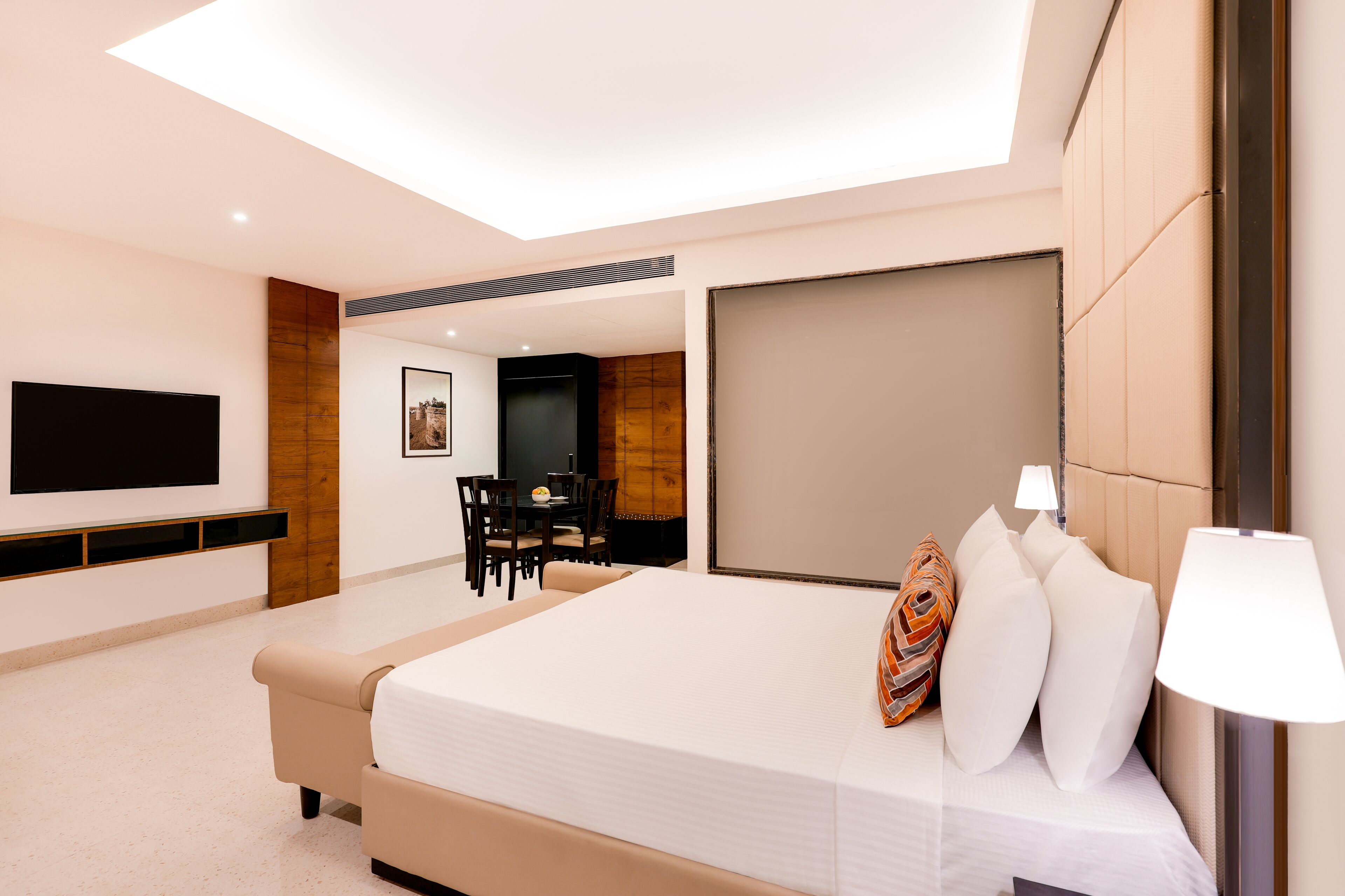 Een moderne hotelkamer met een groot bed, een flatscreen televisie aan de wand, een zithoek met een tafel en stoelen, en een groot raam.