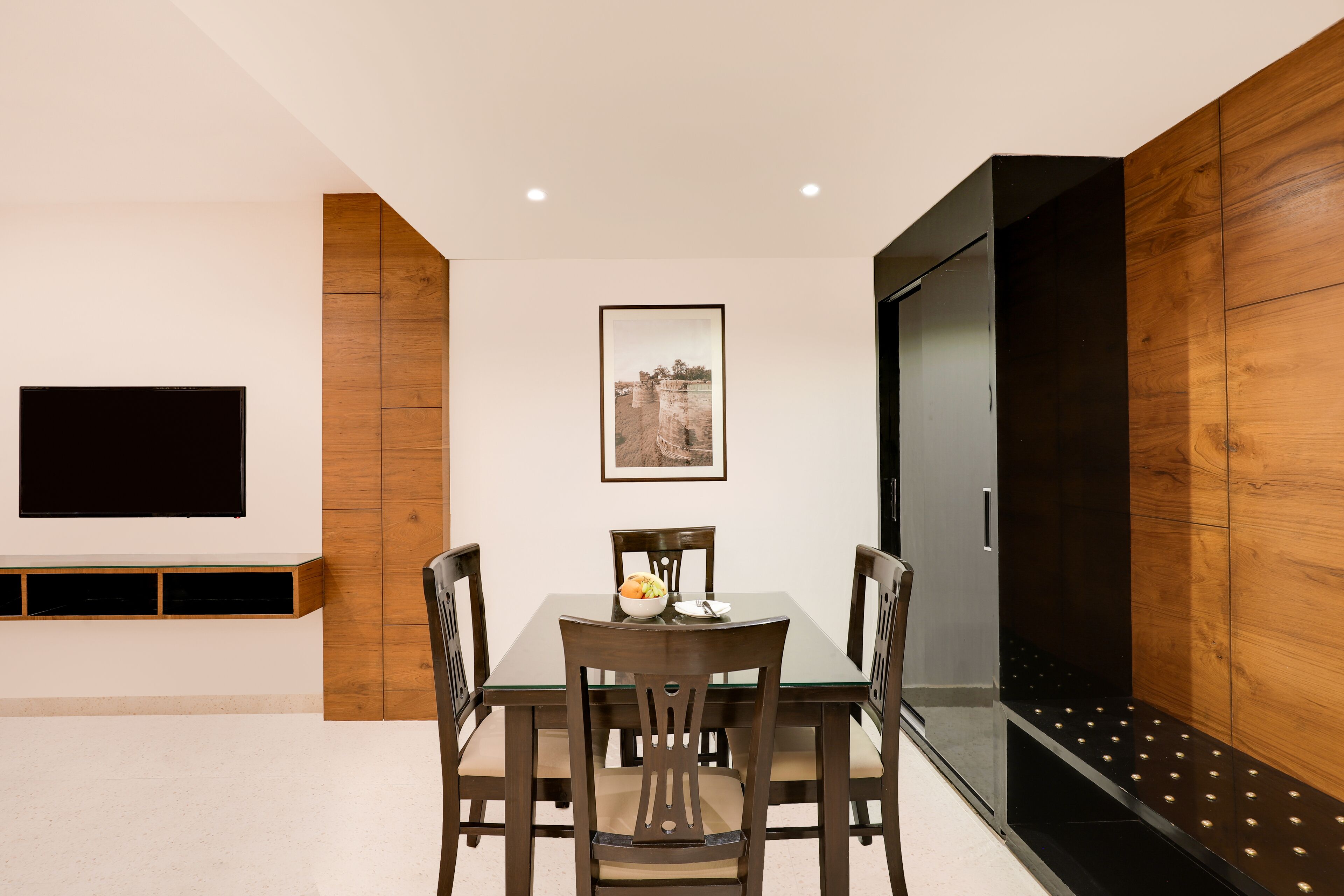 A dining area with a table and chairs, a flat-screen TV mounted on the wall, and a framed picture above the table.