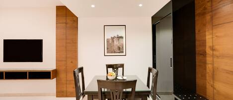 A dining area with a table and chairs, a flat-screen TV mounted on the wall, and a framed picture above the table.