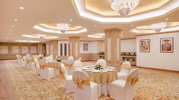 A banquet hall with round tables, white chairs with gold sashes, chandeliers, and framed artwork on the walls.