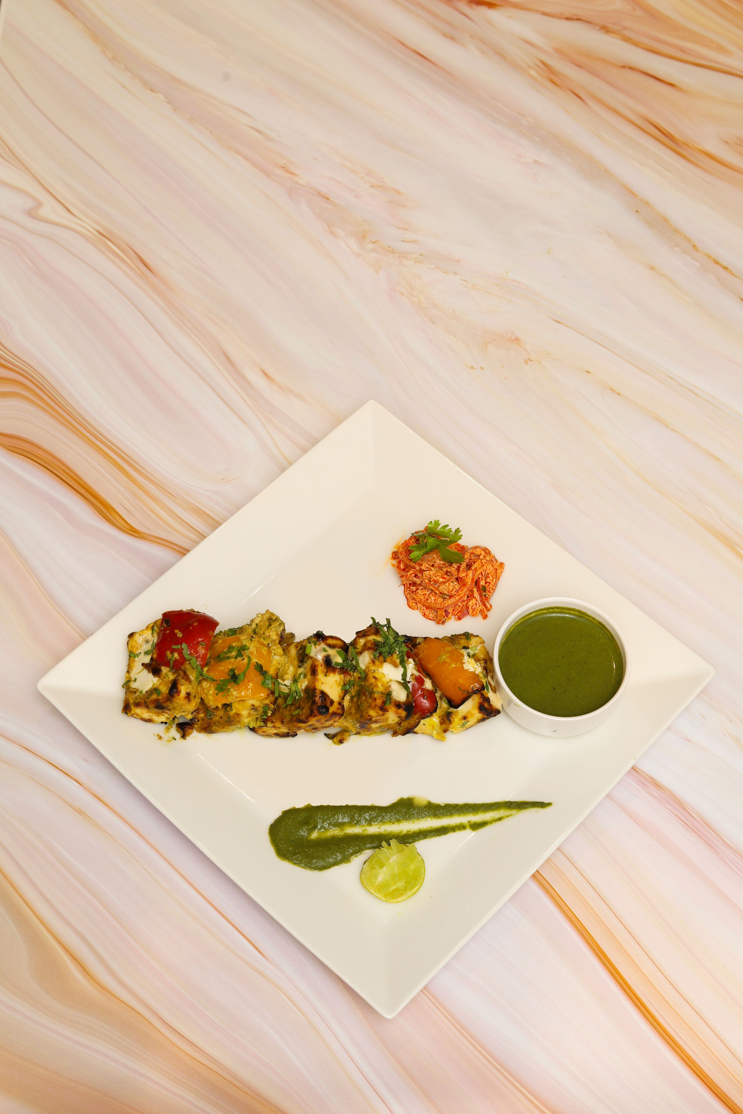 A white plate with a dish of food, a green sauce, and a lime wedge on a marble surface.