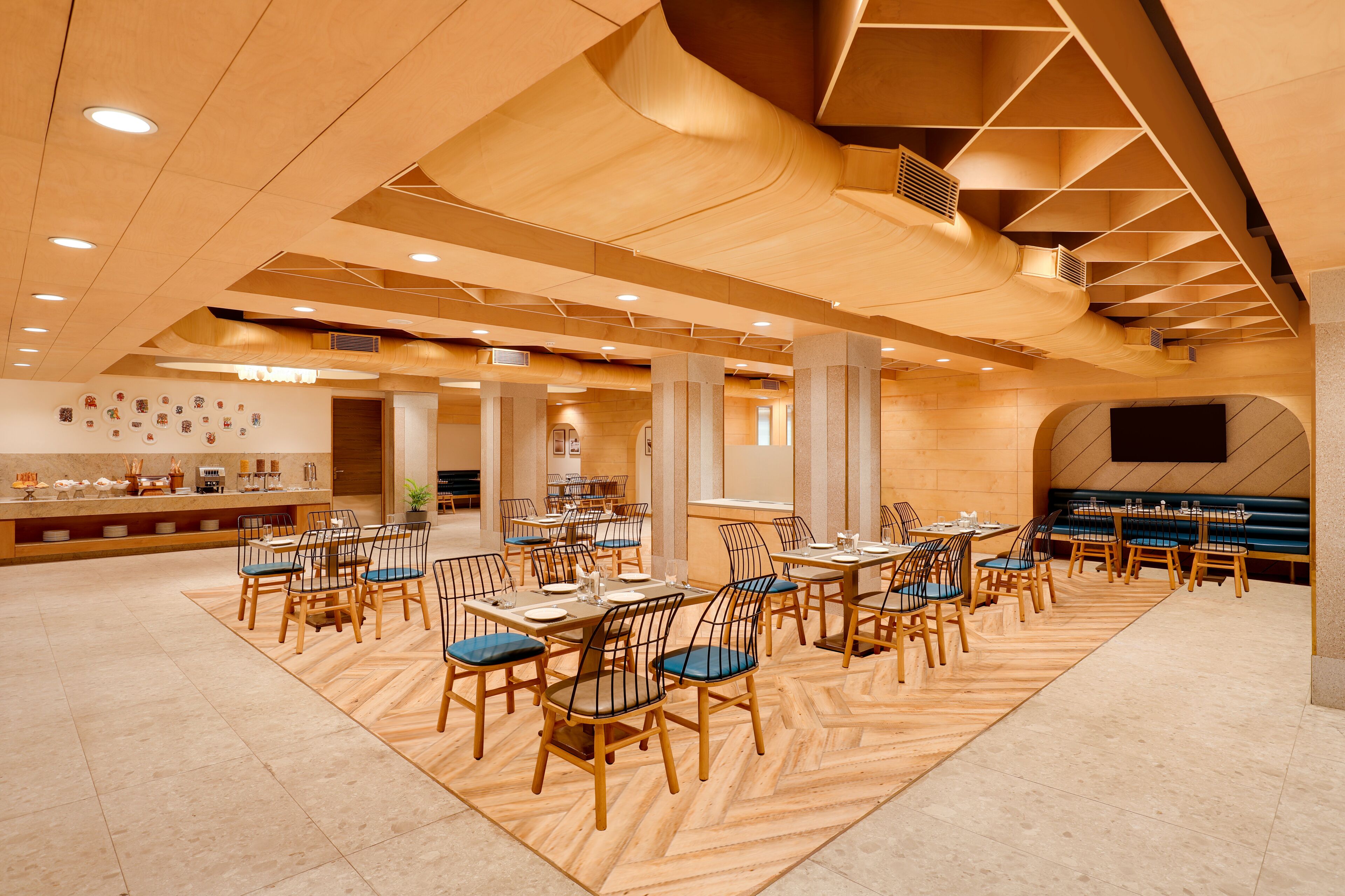 Un restaurante espacioso con suelo de madera, varias mesas y sillas, y un diseño de techo moderno.