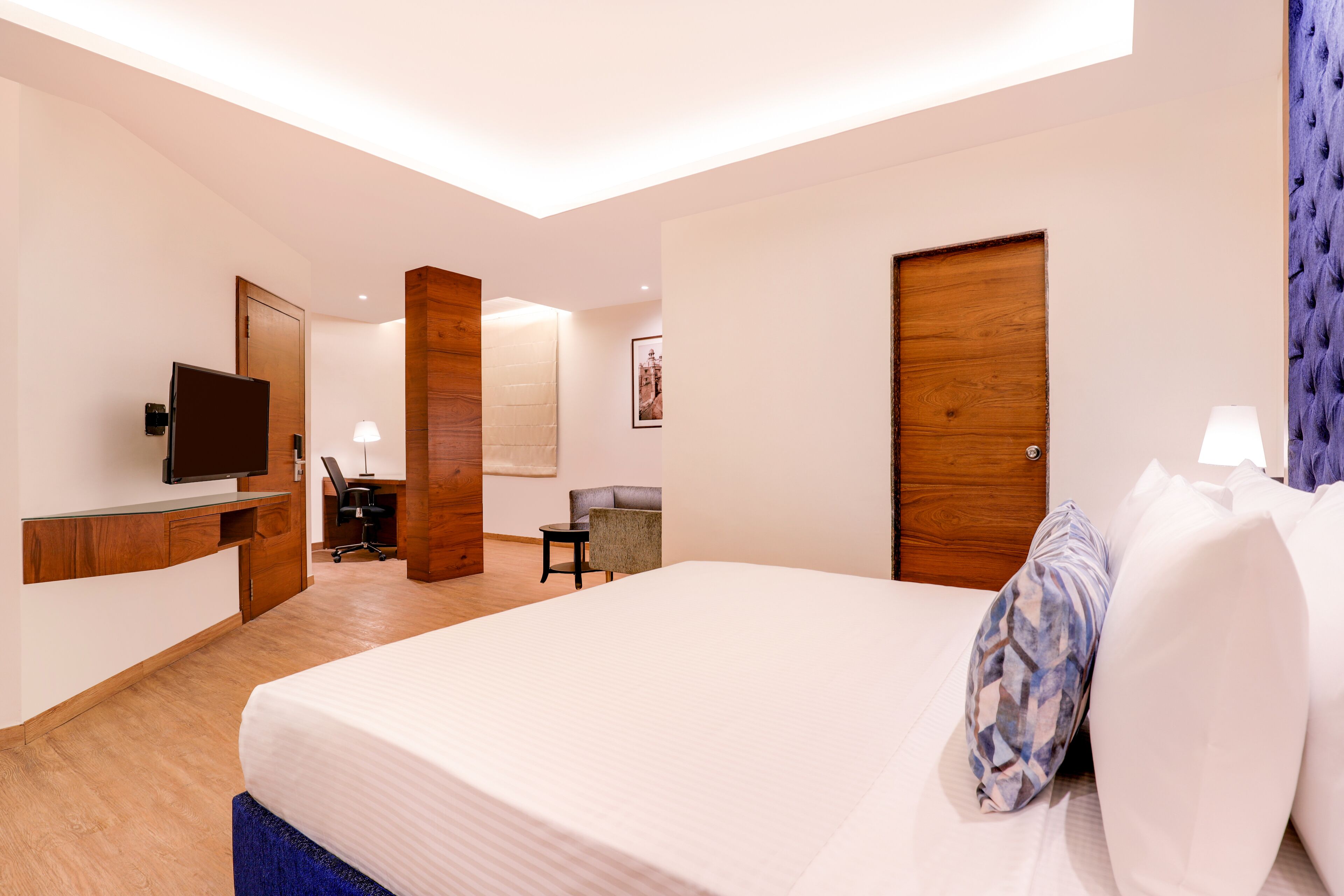 A hotel room with a bed, a desk, a chair, a television, and a door.