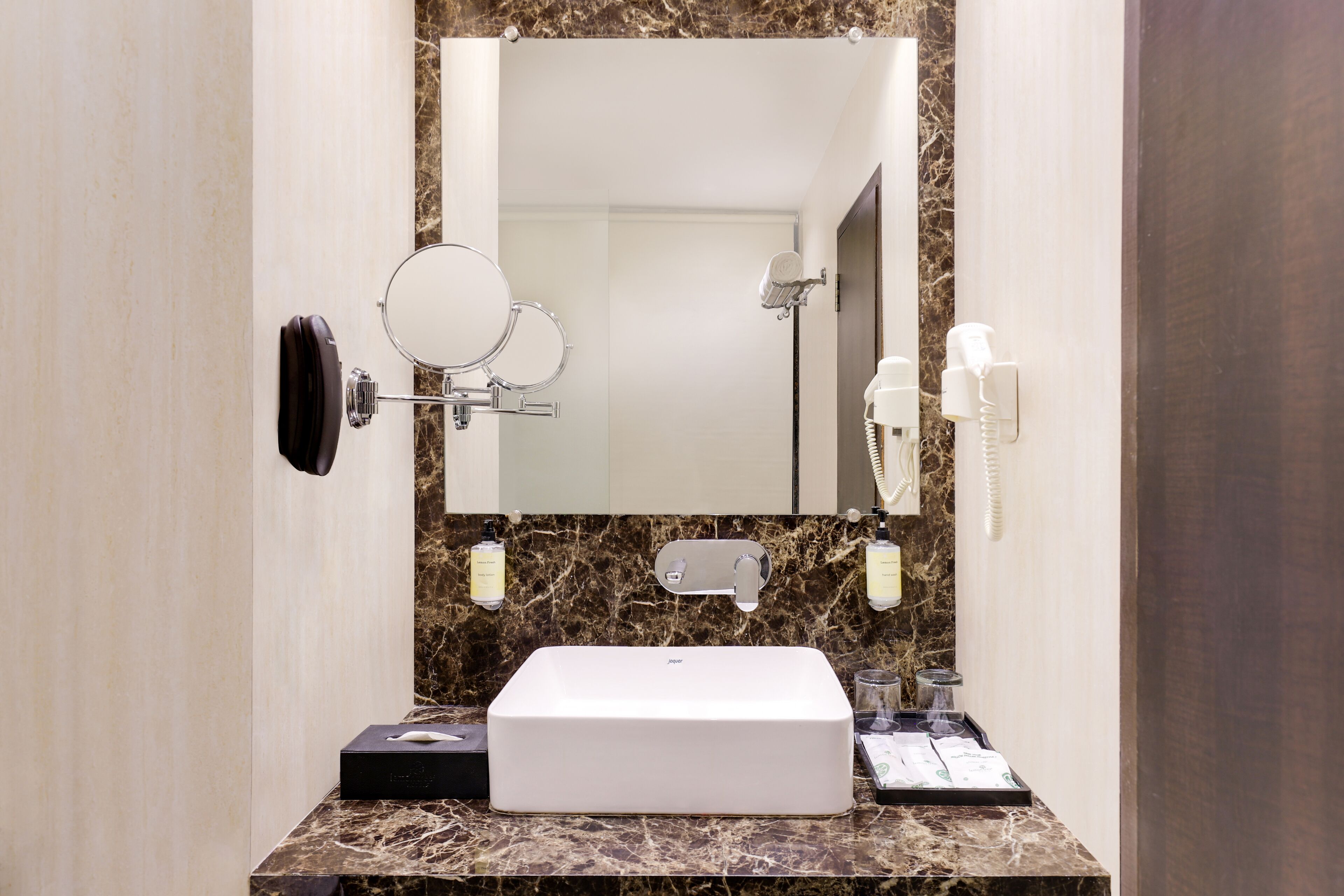 A bathroom with a white sink, a mirror, a hairdryer, and a towel dispenser.