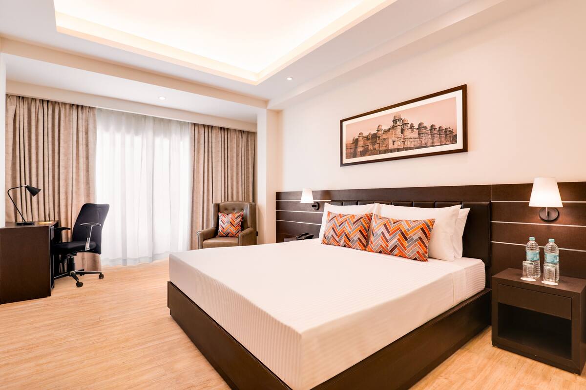 Una habitación de hotel con una cama grande, un escritorio, una silla y una mesita de noche con lámparas.