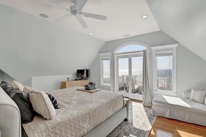 Une chambre avec un grand lit, une télévision, un ventilateur de plafond et un balcon avec vue.