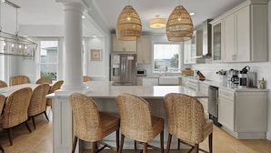 A modern kitchen with a central island, white cabinetry, and wicker chairs. - Moondance | Oceanfront | Private Heated Pool & Hot Tub (North Topsail Beach)