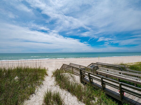 A wooden boardwalk leading to a sandy beach with a clear view of the ocean.