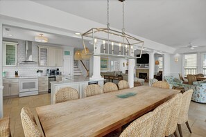A spacious kitchen with white cabinetry, a wooden dining table, wicker chairs, and a hanging light fixture.