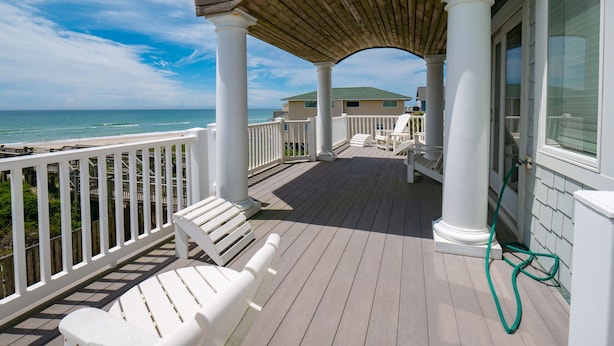 A covered deck with white railings and benches, overlooking a beach. - Moondance | Oceanfront | Private Heated Pool & Hot Tub (North Topsail Beach)