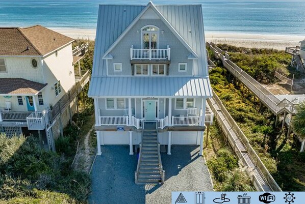 Une maison à deux étages dotée d’un balcon, d’un escalier menant à l’entrée et offrant une vue sur la plage.