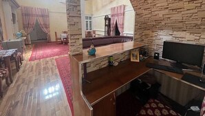 A living room with a stone wall, a sofa, a TV, and a dining area with a table and chairs. - Shodlik Guest House (Khiva)
