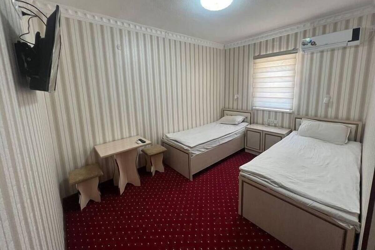Een kleine hotelkamer met een gestreept behang, een rood tapijt, een bed, een bureau en een garderobe.
