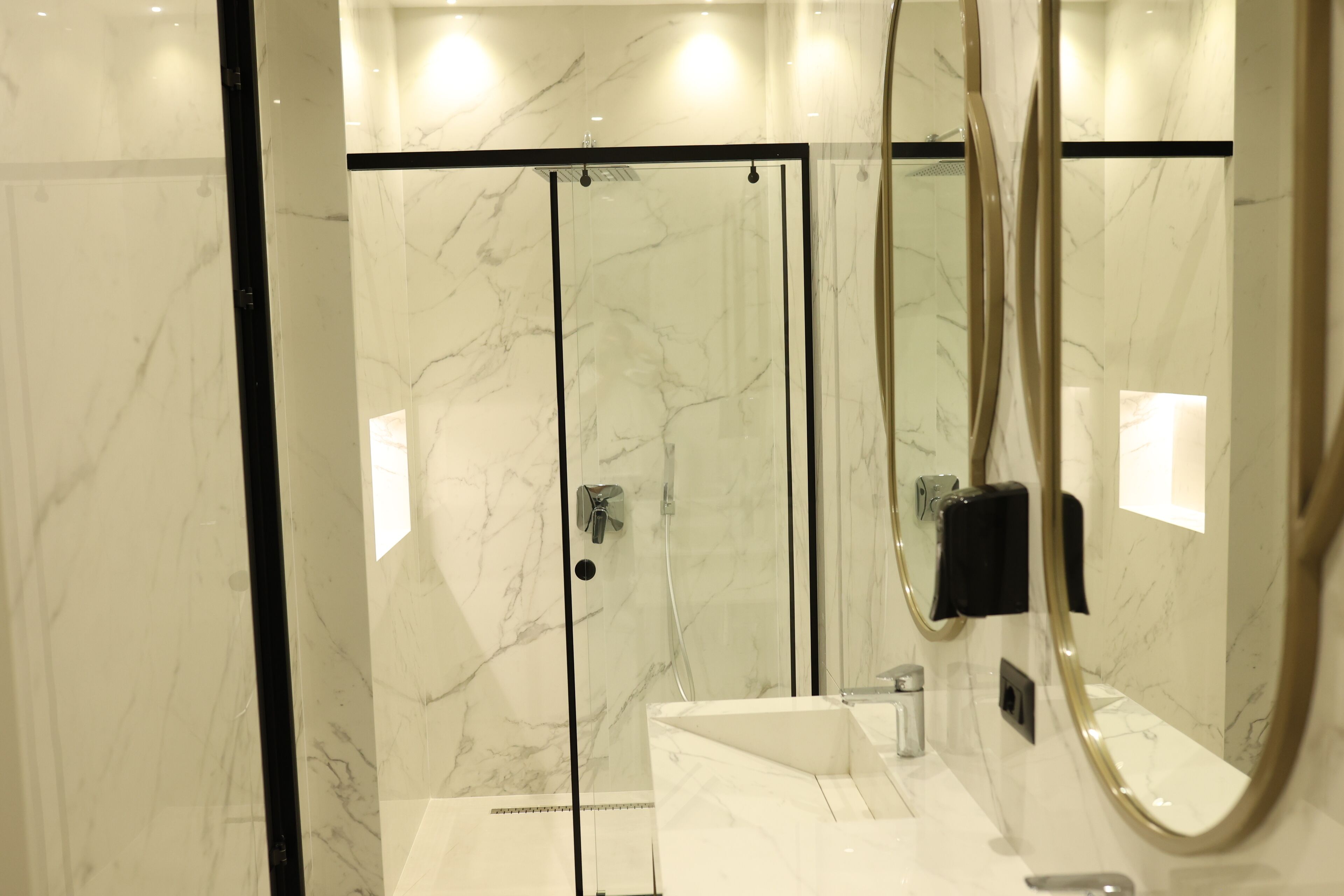 A modern bathroom with a glass-enclosed shower, a white marble sink, and a large mirror.