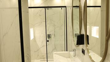 A modern bathroom with a glass-enclosed shower, a white marble sink, and a large mirror.