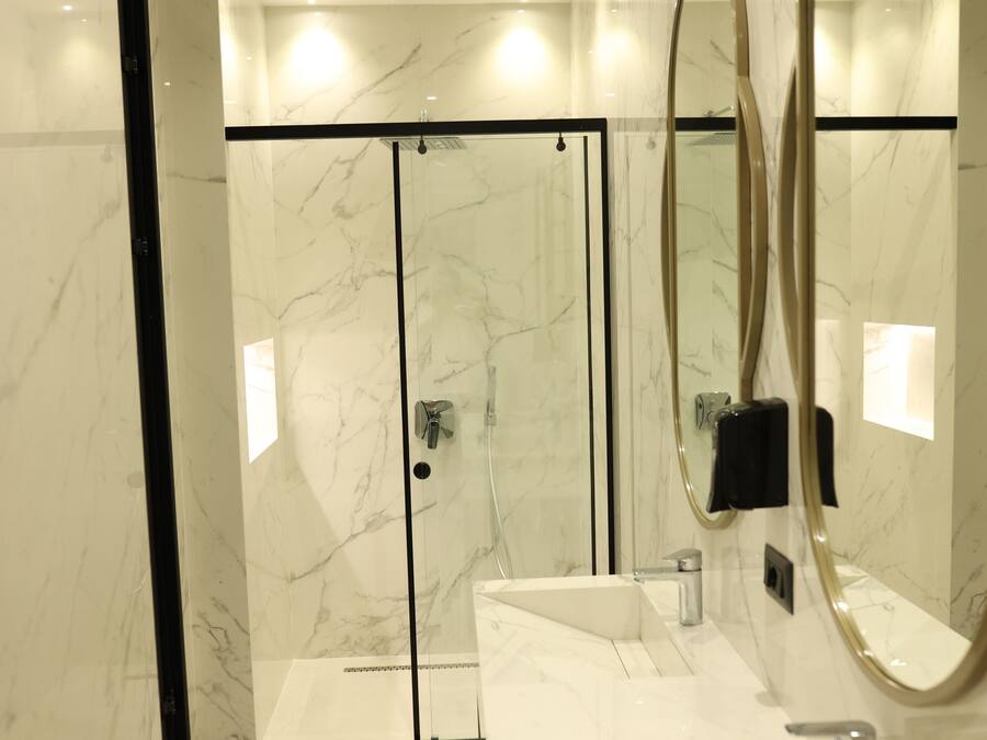 A modern bathroom with a glass-enclosed shower, a white marble sink, and a large mirror.