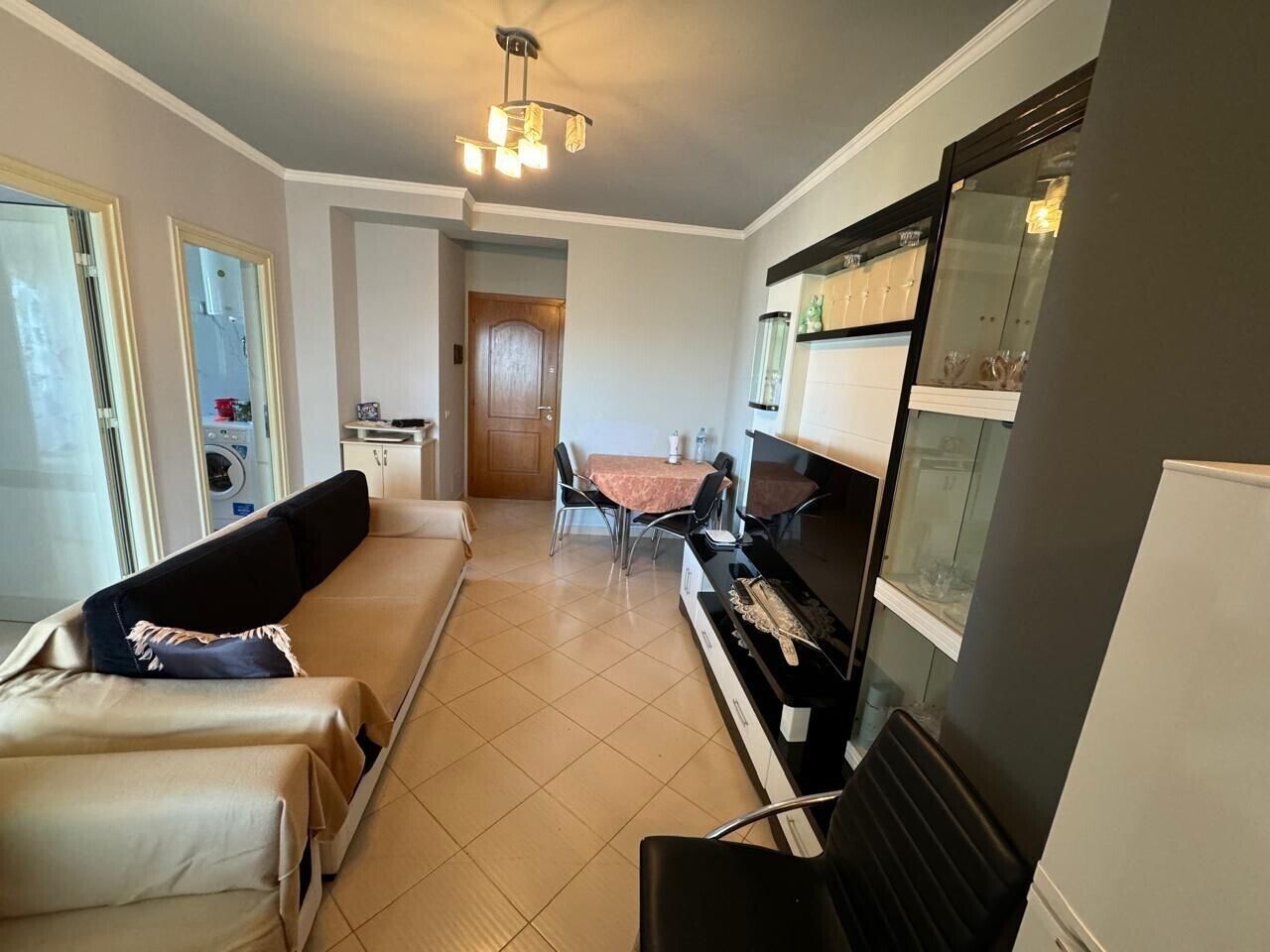 A compact living space with a sofa, dining table, kitchenette, and a glass-fronted cabinet.