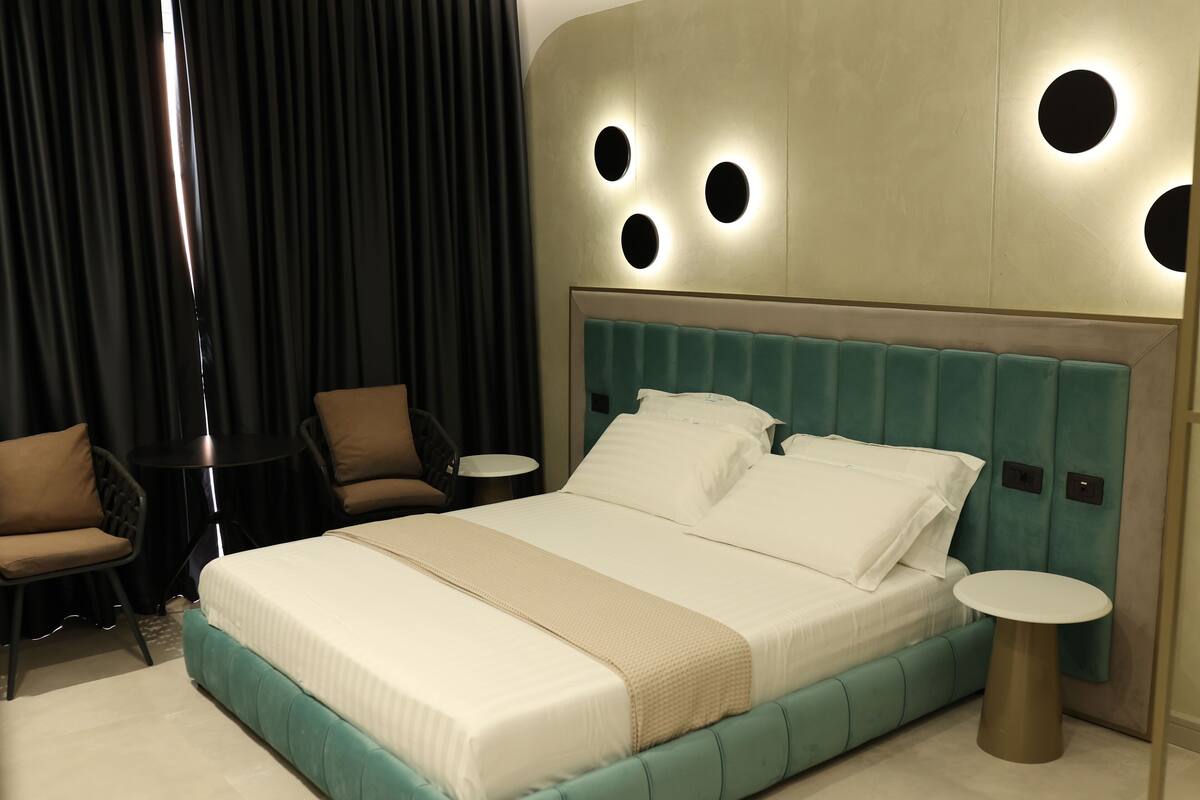 A modern hotel room with a large bed, two side tables, a chair, and a curtain.
