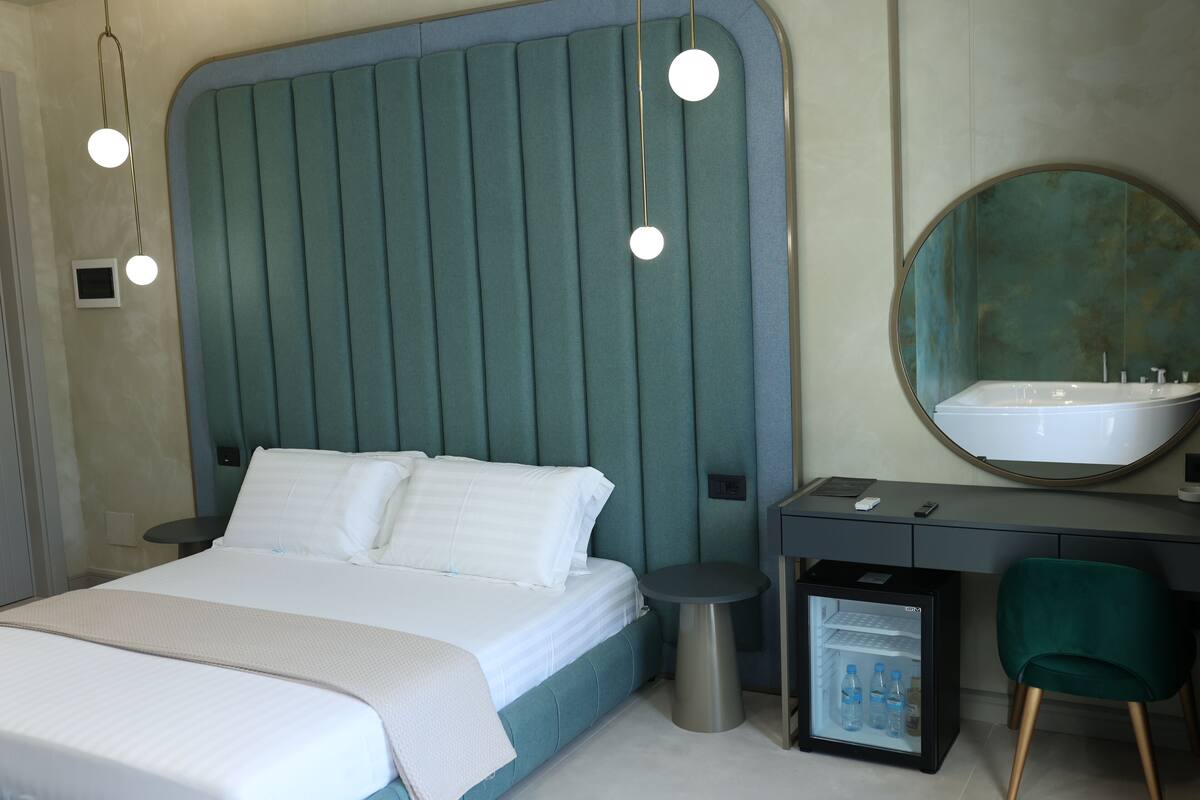 A modern bedroom with a large bed, bedside tables, a small fridge, and a mirror.