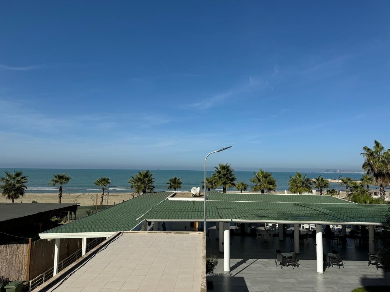 Una terraza en la azotea con vista a la playa, palmeras y un cielo despejado.