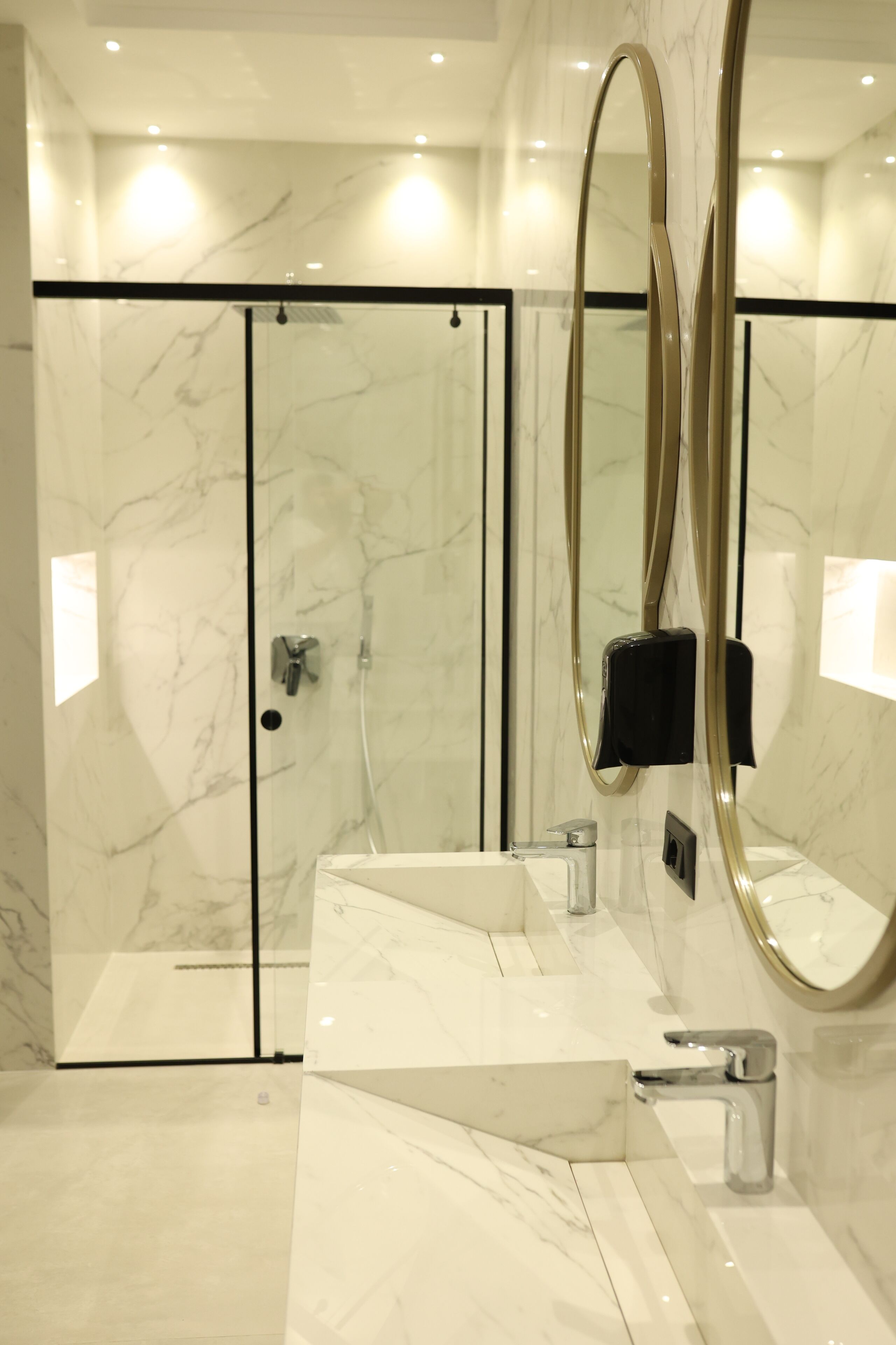 A modern bathroom with a glass-enclosed shower, a white marble sink, and a large mirror with a gold frame.