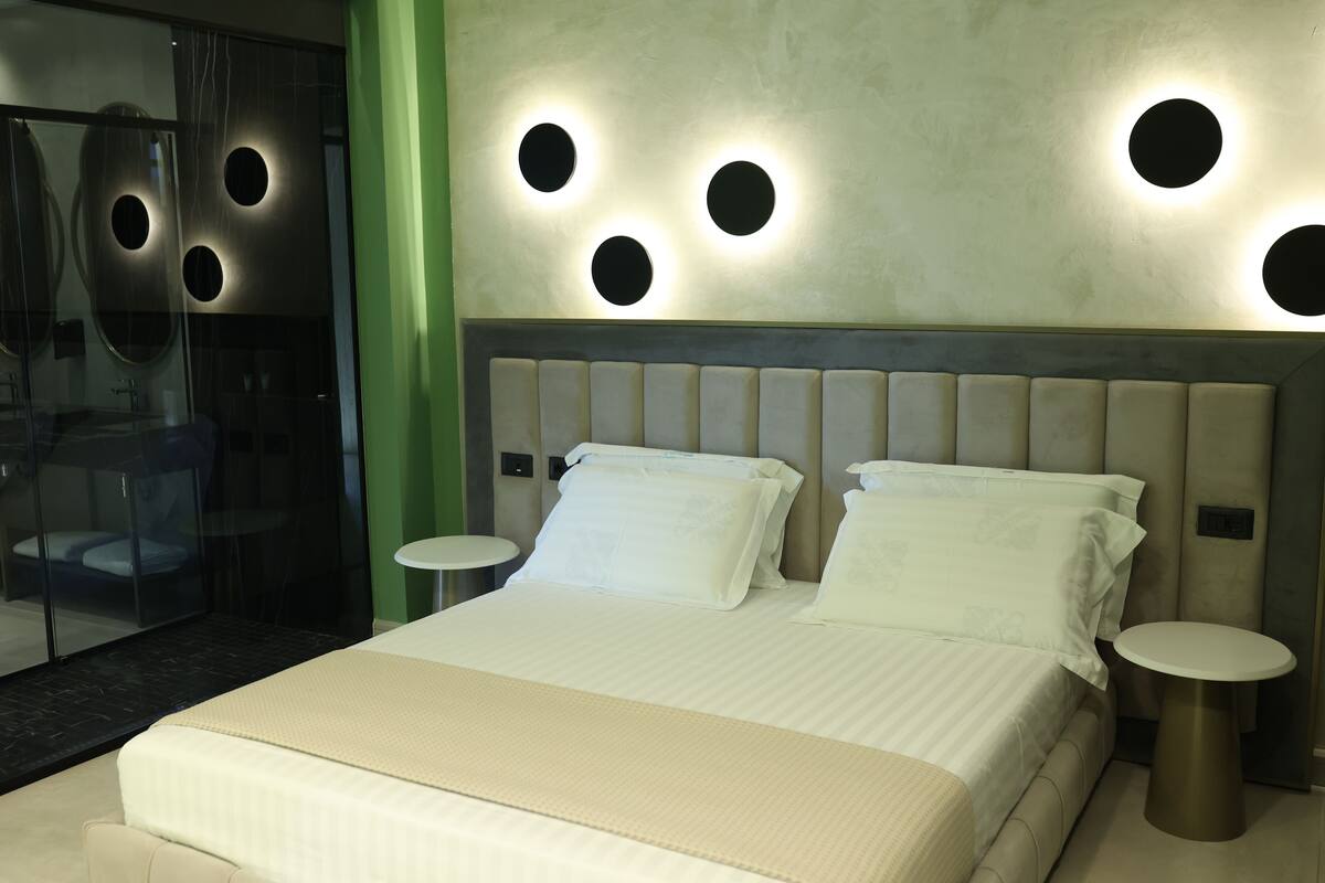 A hotel room with a large bed, two bedside tables, and a modern wall design with circular light fixtures.