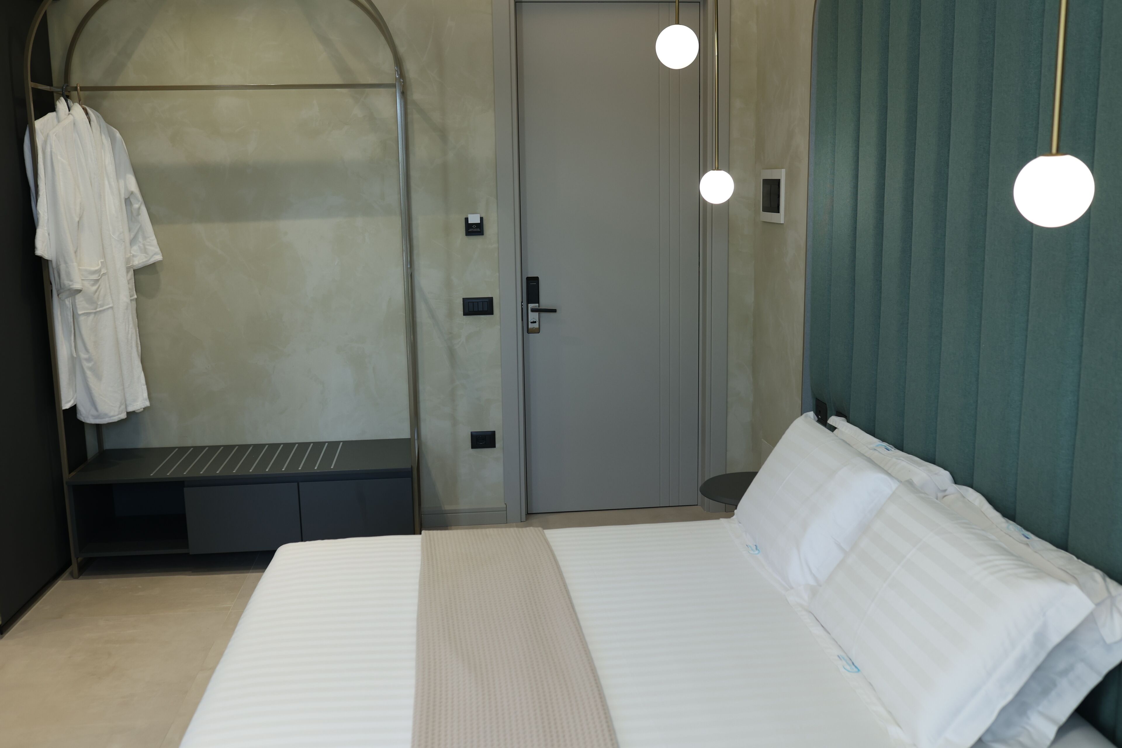Een moderne hotelkamer met een groot bed, een bank met badjassen, een deur en hanglampen.