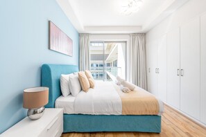 A modern bedroom with a bed, a nightstand, a lamp, and a view of a balcony. - Luxury Beachfront Marjan Island (Ras Al Khaimah)
