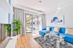 Ein modernes Wohnzimmer mit einem blauen Sofa, einem Glastisch und einem großen Fenster mit Vorhängen.