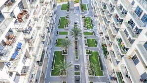 Um edifício residencial alto com várias varandas, um pátio central com palmeiras e vista para a praia ao fundo.