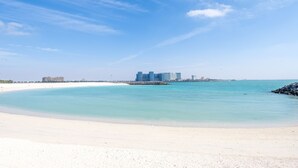 Uma praia com águas turquesa cristalinas, uma faixa de areia e uma vista distante de um complexo hoteleiro.