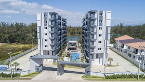 A modern apartment complex with a central swimming pool, surrounded by greenery and a clear sky.
