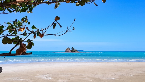 A beach with clear blue water, a sandy shore, and a small island with vegetation in the distance.