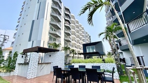 A modern apartment building with multiple balconies, a patio area with outdoor furniture, and a stone wall.