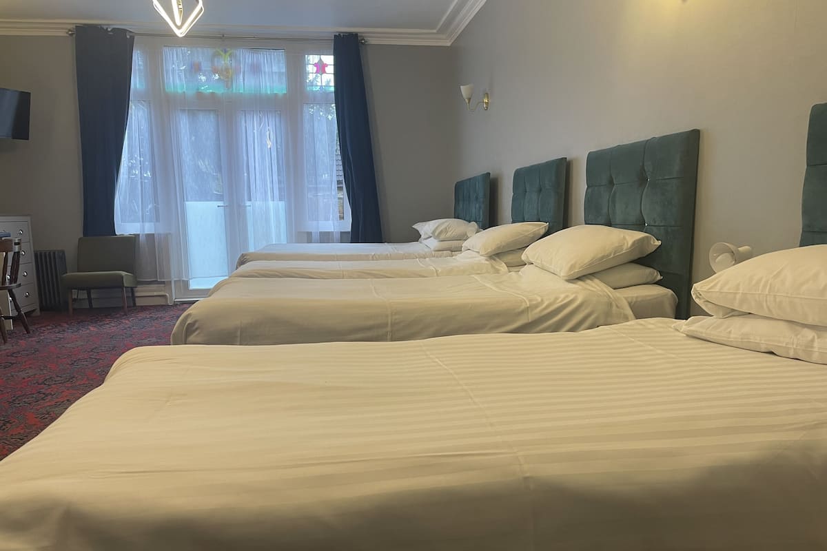 Ein Hotelzimmer mit drei Betten, einem Fernseher, einem Sessel und einem Fenster mit Vorhängen.