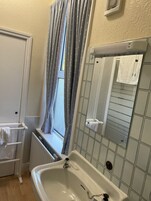 Un baño con bañera, una ventana con cortinas, un perchero para toallas y un muro con azulejos.