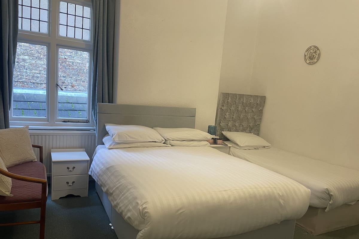 Ein Schlafzimmer mit einem großen Bett, zwei Nachttischen, einem Sessel und einem Fenster mit Vorhängen.
