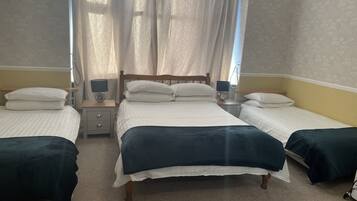 A hotel room with two single beds, a wooden headboard, a nightstand with a lamp, and a window with curtains.