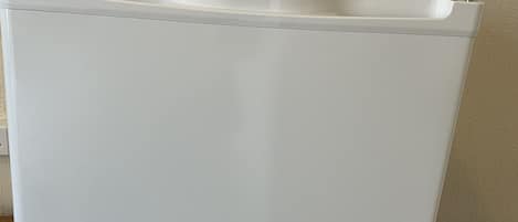 A white, rectangular, plastic storage bin with a lid, placed on a wooden surface against a textured wall.