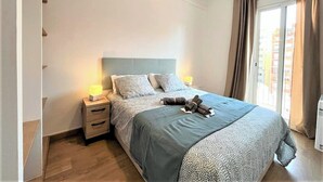A bedroom with a bed, bedside lamps, a nightstand, a window with curtains, and a ceiling light fixture.