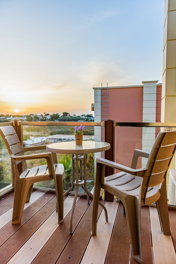 A balcony with a round table and four chairs, overlooking a cityscape during sunset.